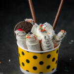 side view of thai ice cream roll topped with colorful sprinkles in a cardboard bowl on black background